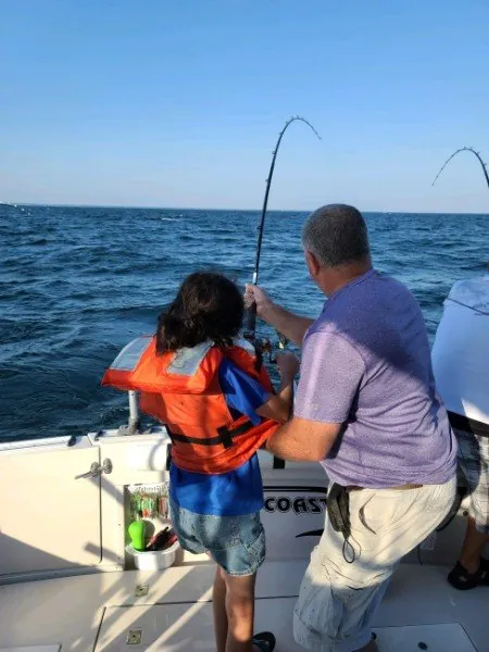 A young angler in a life jacket fighting a fish with the captain beside him